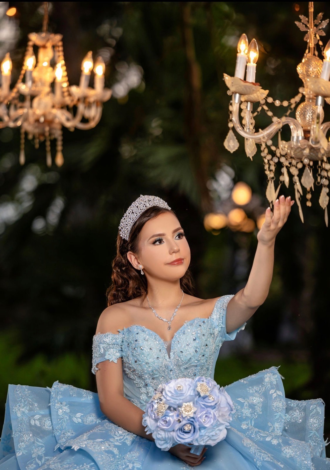 Carolina reaching toward a glowing chandelier with her bouquet