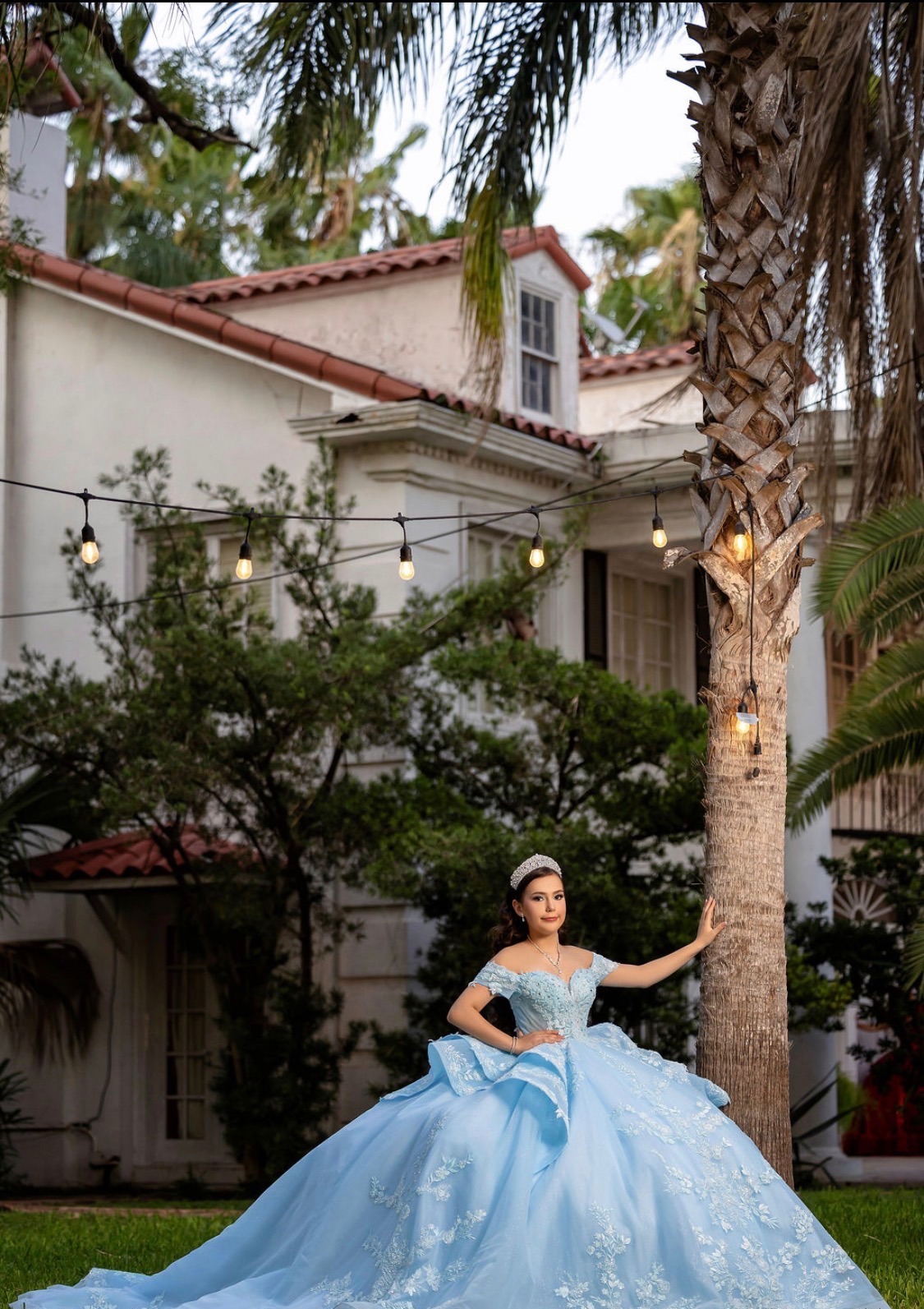 Carolina beside a palm tree under string lights at the mansion