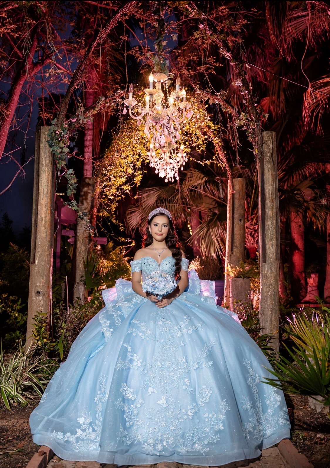 Carolina seated beneath a chandelier in a candlelit garden arch