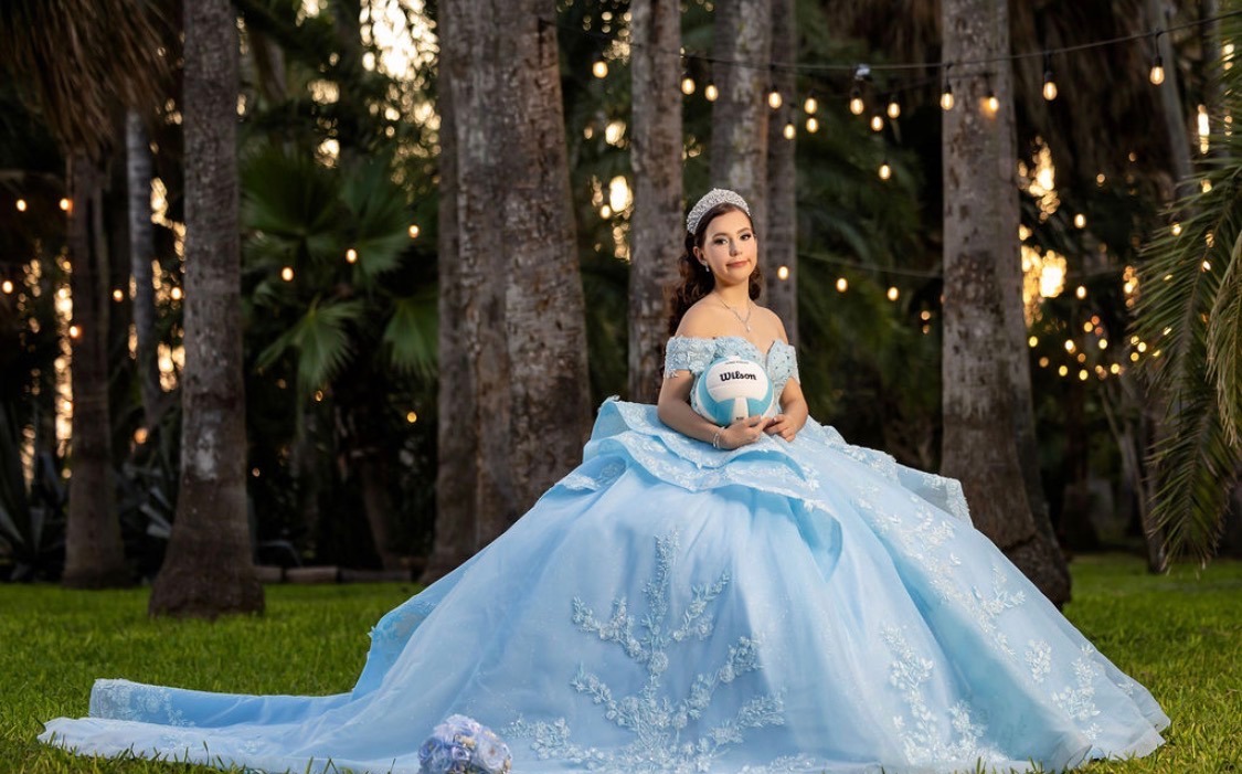 Carolina holding a volleyball in her ball gown among the palms